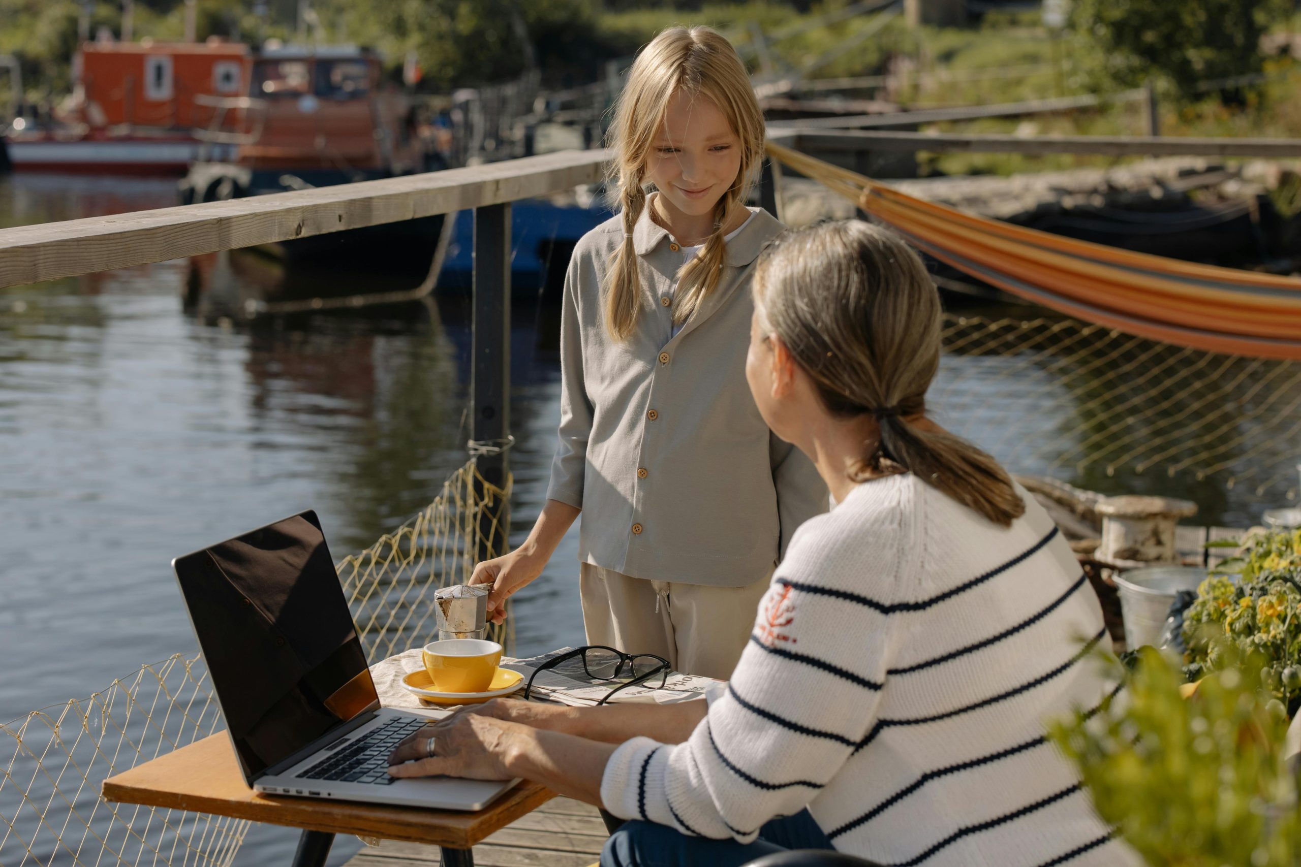 pexels-photo-7047423-7047423 Mother and daughter working with a laptop on a dock by the lake, enjoying the outdoors.
